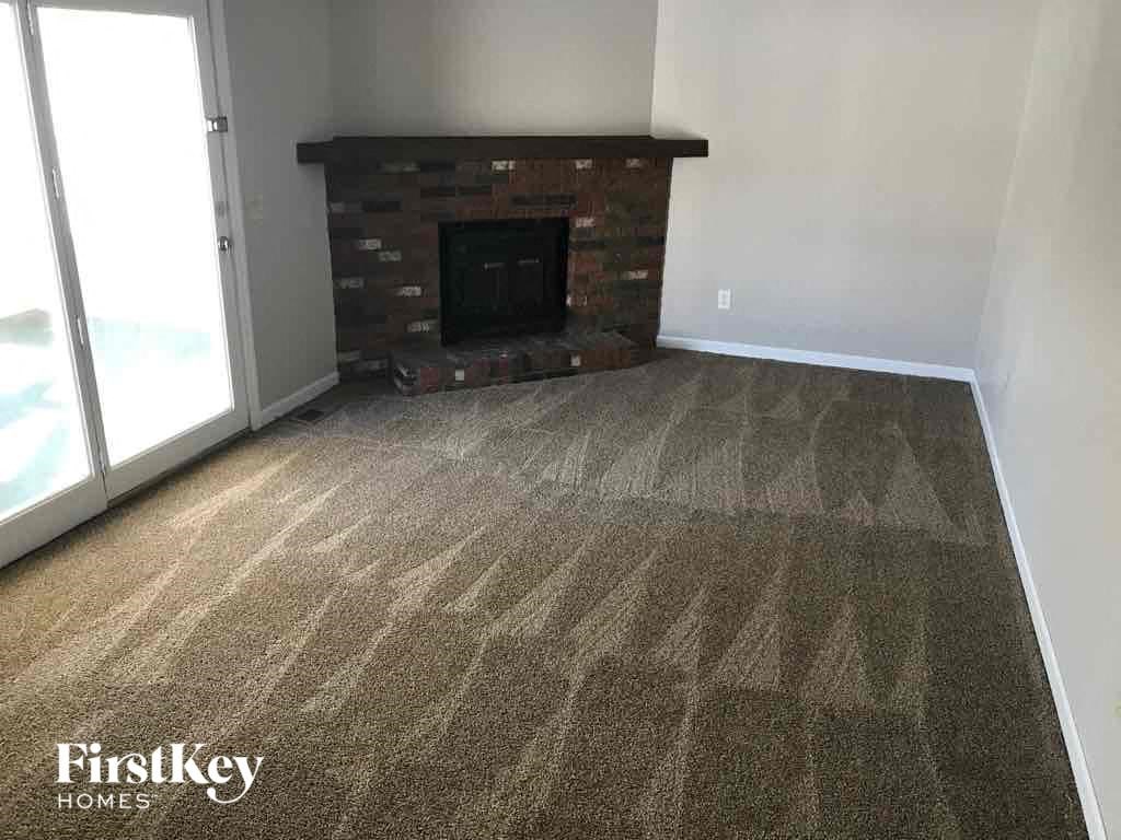 A carpeted room with a fireplace and a door leading outside.