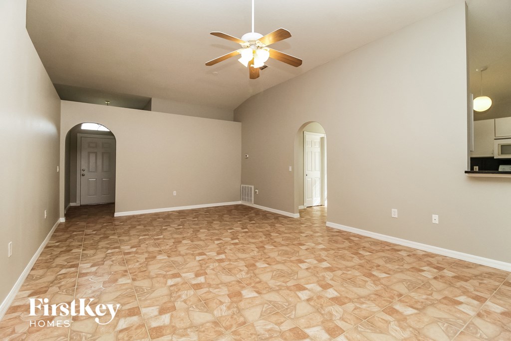an empty living room with a ceiling fan and a door to the kitchen