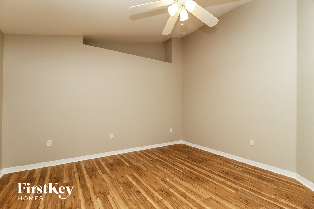 the spacious living room with hardwood flooring and a ceiling fan