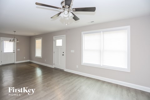 an empty living room with a ceiling fan and two windows