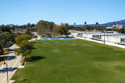 A large grassy field with a swimming pool and buildings in the background.