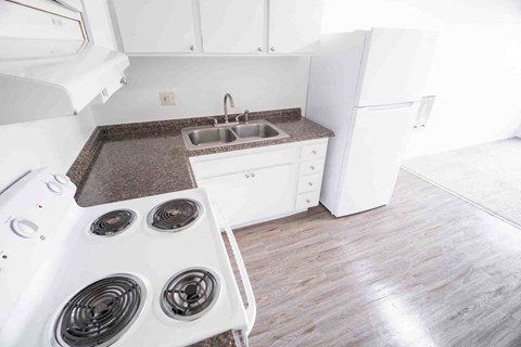 A white stove top oven with four burners sits next to a kitchen counter with a sink.