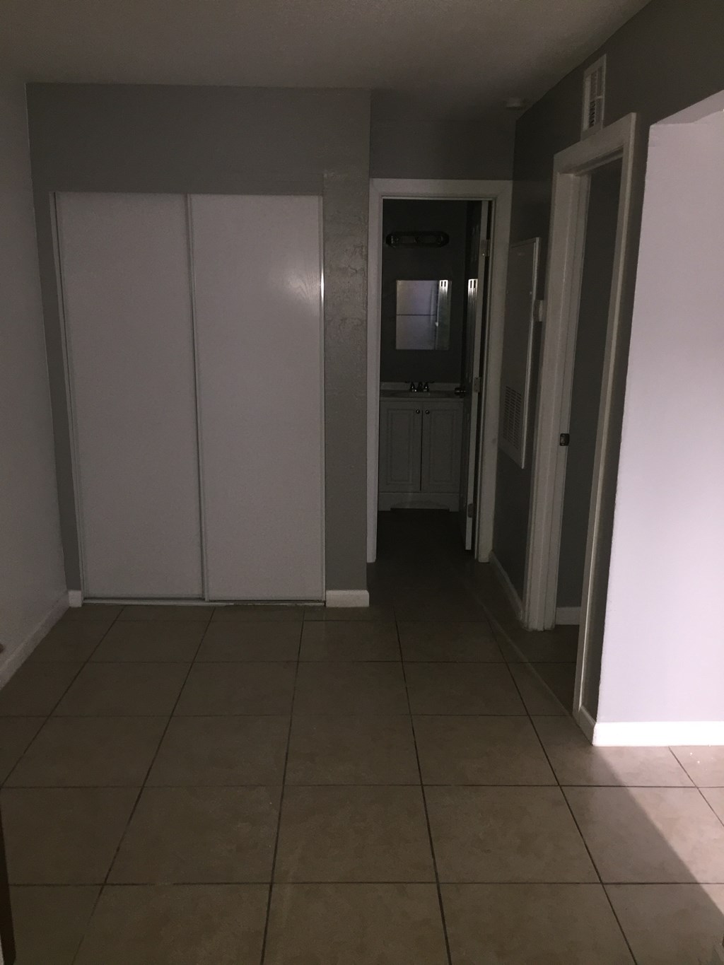 a hallway with white walls and a tiled floor and a door to a bathroom