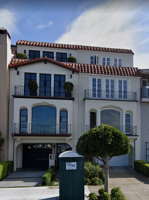 A two-story house with a balcony and a tree in front.