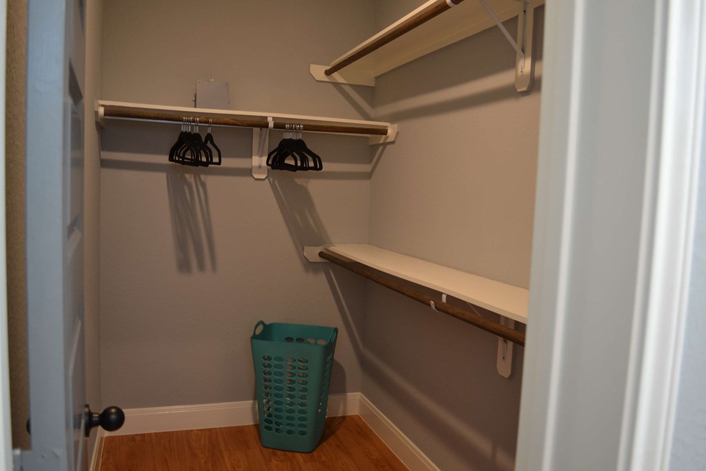 a walk in closet with a shelf and a trash can