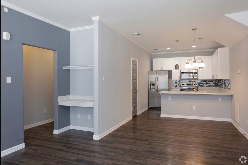 an empty living room and kitchen with a refrigerator and microwave