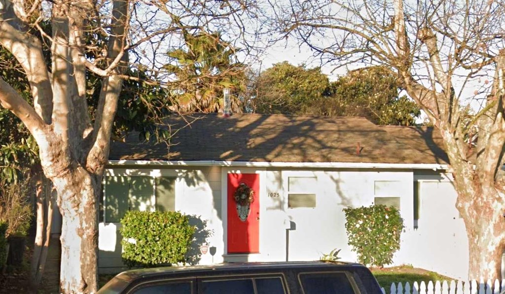 A white house with a red door is surrounded by trees.