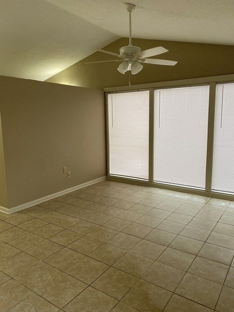 an empty living room with a ceiling fan and windows