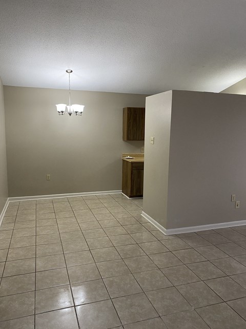 an empty living room with a tiled floor and a kitchen