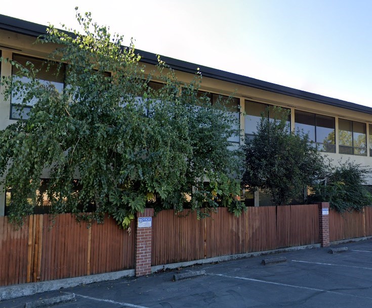 A building with a wooden fence and greenery in front.