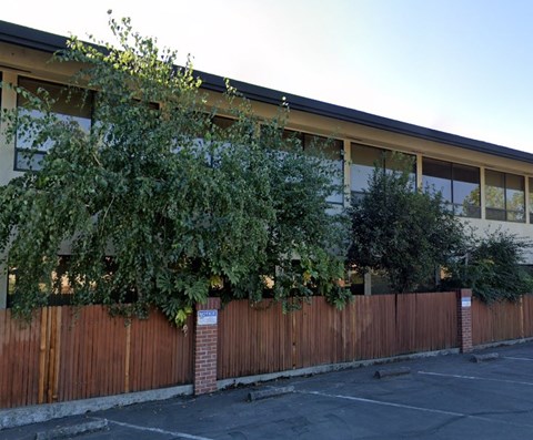 A building with a wooden fence and greenery in front.