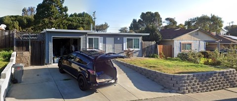 A black car is parked in a driveway outside a house.