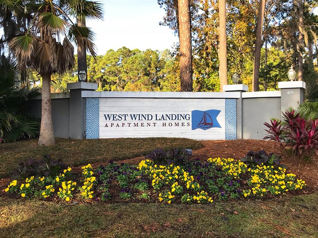 a sign for the westwind landing apartment homes in front of trees and flowers