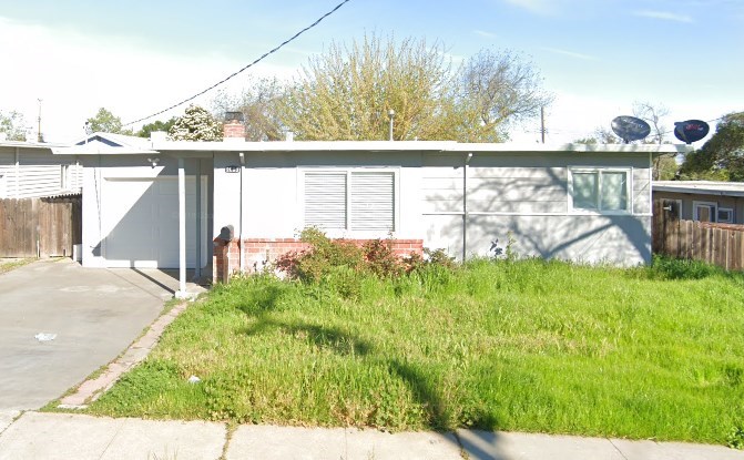 A white house with a grey garage door is surrounded by grass and trees.