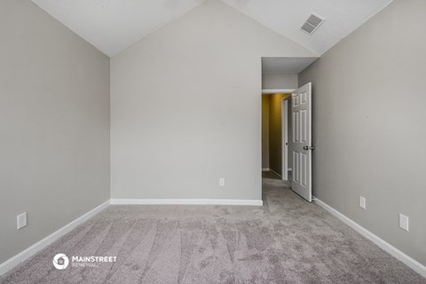 the living room of an apartment with carpet and a door to the hallway