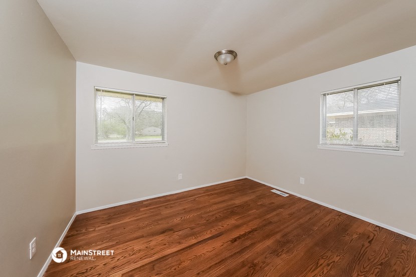 the bedroom with hardwood flooring and two windows