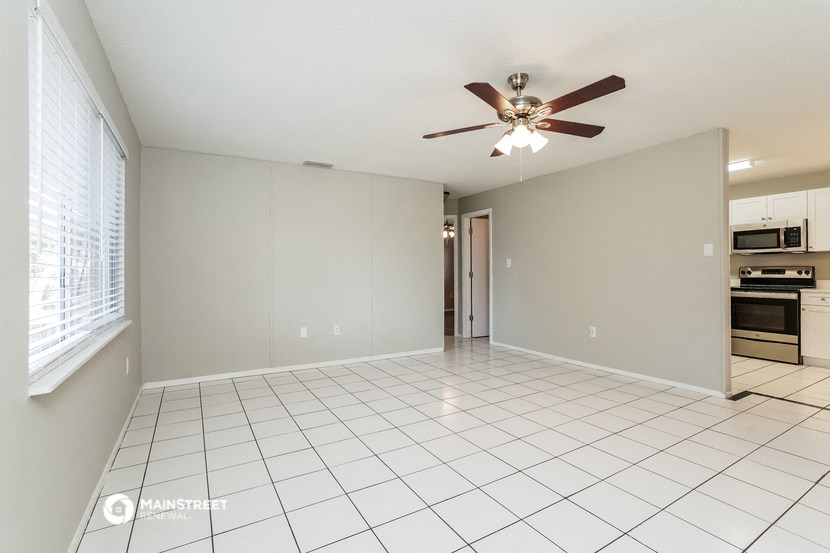 an empty living room with a ceiling fan and a kitchen