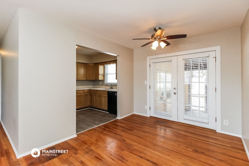an empty living room with a door to the kitchen and a ceiling fan