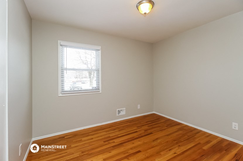 the bedroom of a house with wood flooring and a window