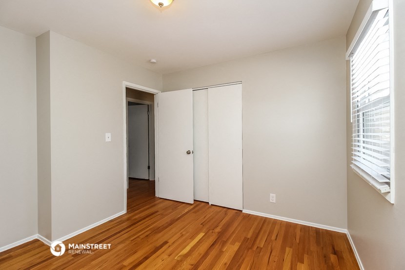 a bedroom with white walls and wood floors and a closet