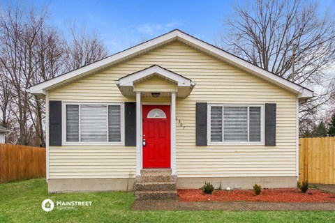 the front of a yellow house with a red door