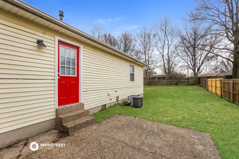 the side of a house with a red door and a backyard