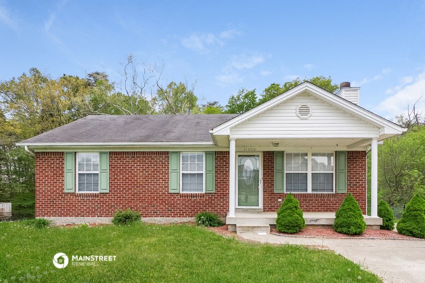 a small brick house with green shutters and a lawn