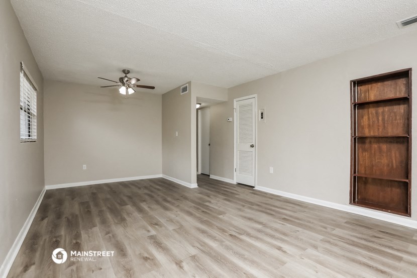 the spacious living room with wood flooring and a ceiling fan