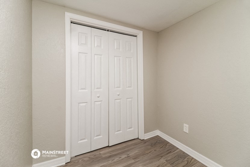 the bedroom of an apartment with white closets and wood flooring