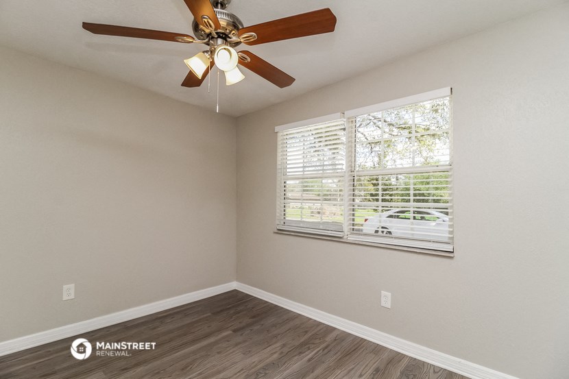 the spacious living room with a large window and a ceiling fan