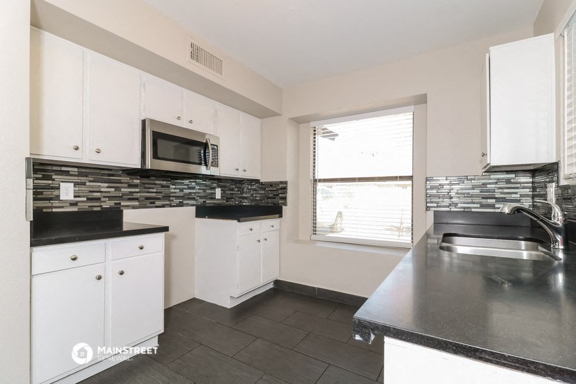 a kitchen with white cabinets and black counter tops and a window