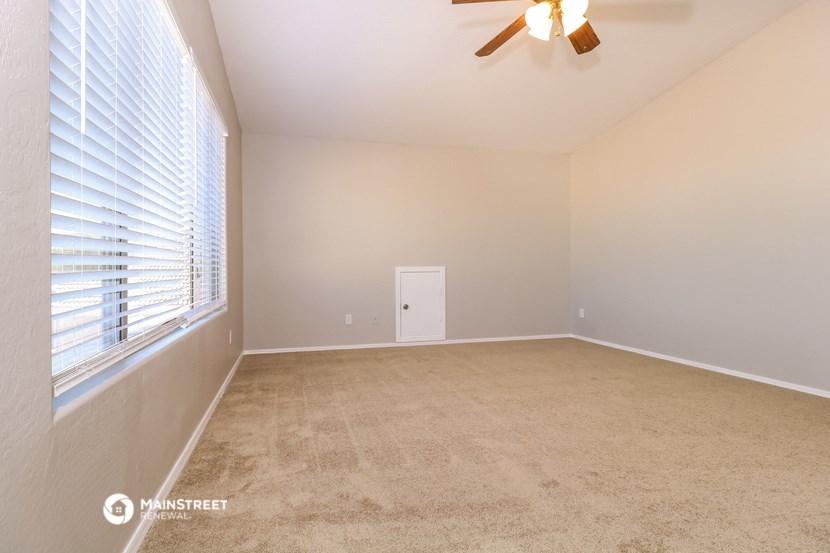 an empty living room with a large window and a ceiling fan