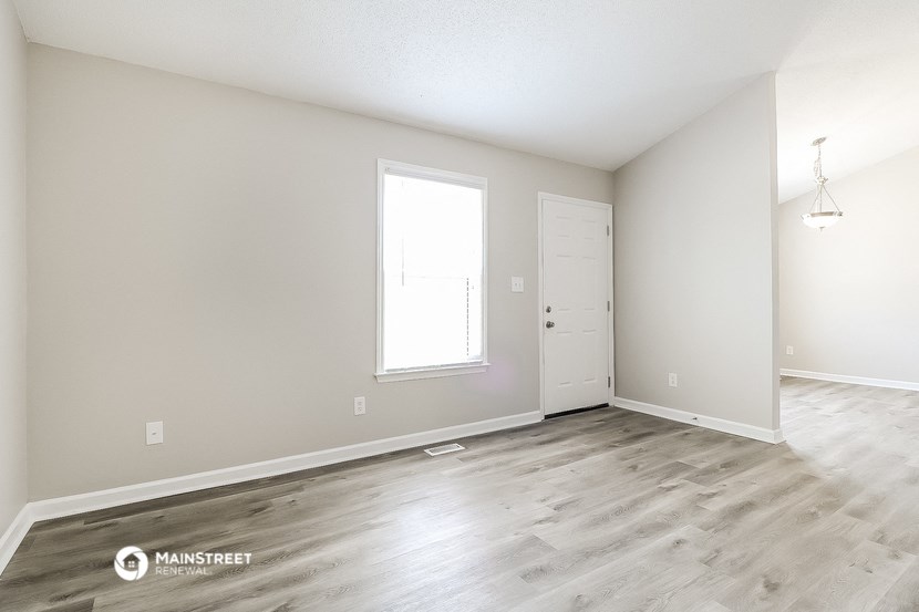 the spacious living room with wood flooring and a door to the bedroom