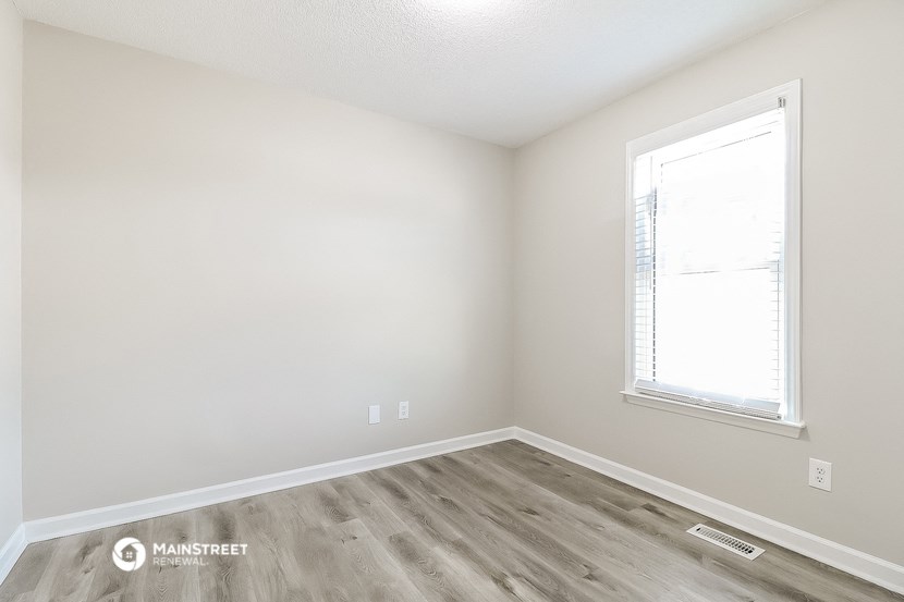 a bedroom with white walls and wood flooring and a window