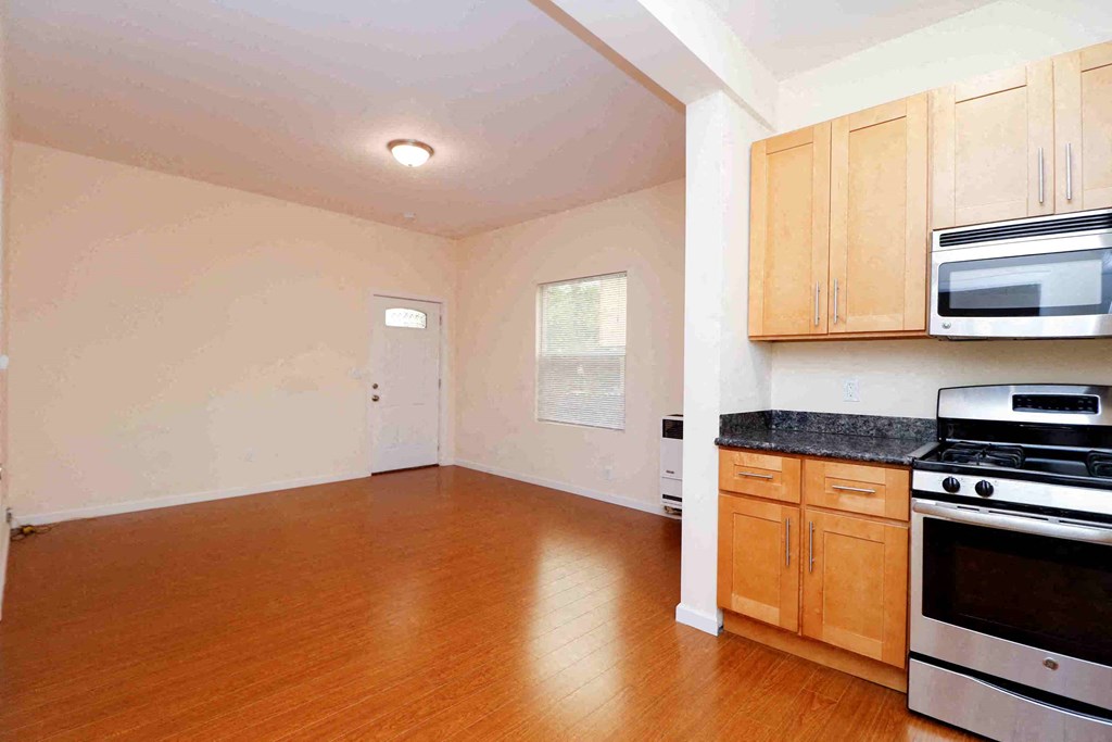 an empty kitchen and living room with wood floors and appliances