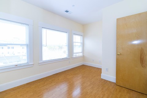 an empty room with a wooden floor and three windows and a wooden door
