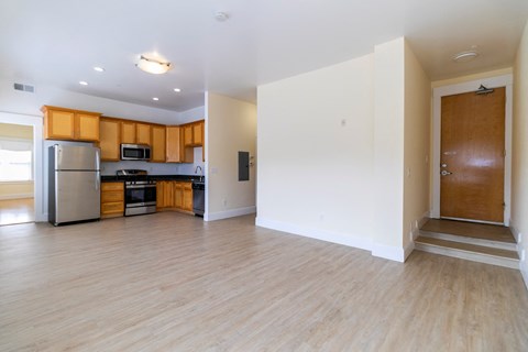 an empty kitchen and living room with wood flooring and a refrigerator
