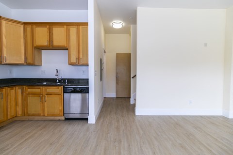 an empty kitchen and living room with wood flooring and wooden cabinets