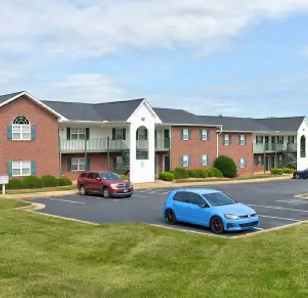 A blue car is parked in a parking lot in front of a red car and a building.
