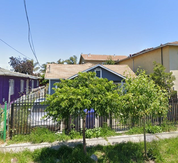 A house with a blue roof is surrounded by a fence and greenery.