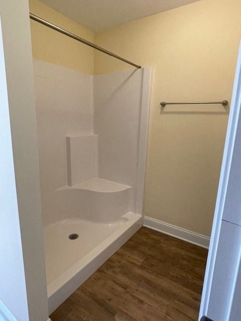 A white bathtub with a shower head is in a bathroom with wood flooring.