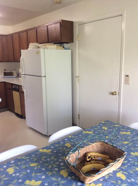 A kitchen with a white fridge and a table with a basket of bananas on it.