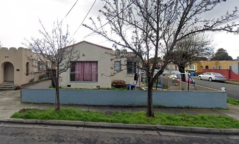 A house with a red curtain on the window and a tree in front of it.