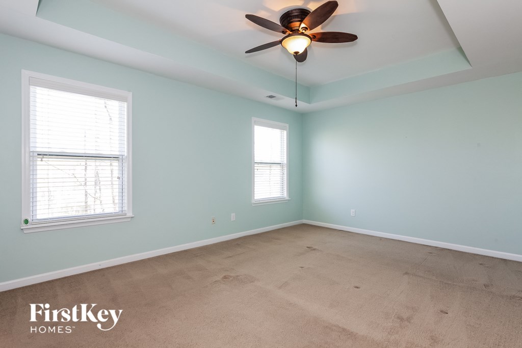 A room with a ceiling fan and two windows.