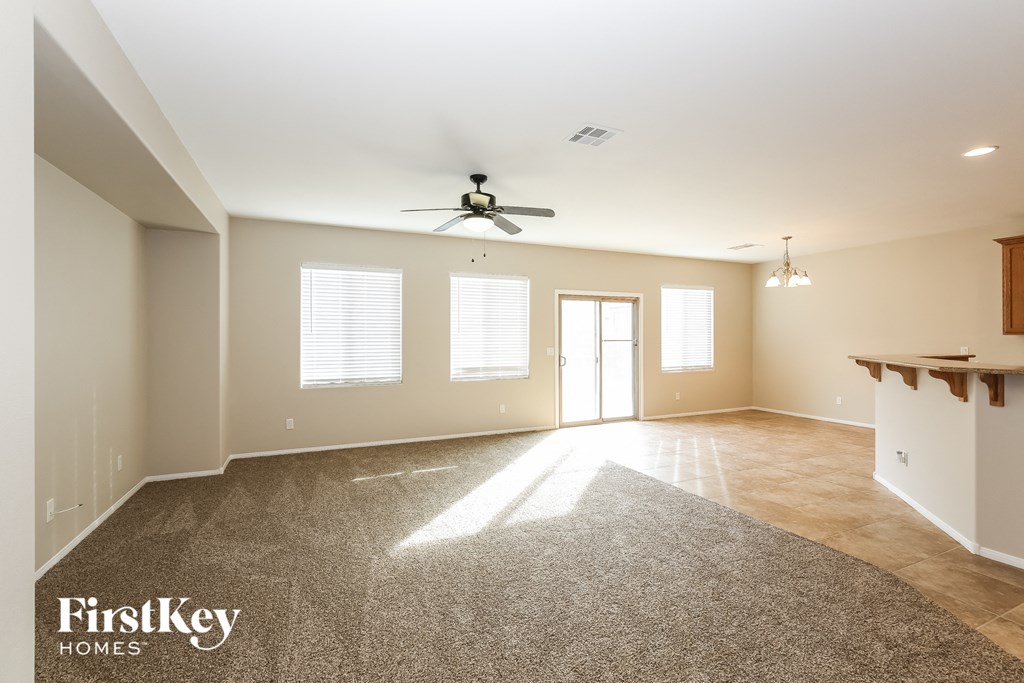 an empty living room with a ceiling fan and a kitchen