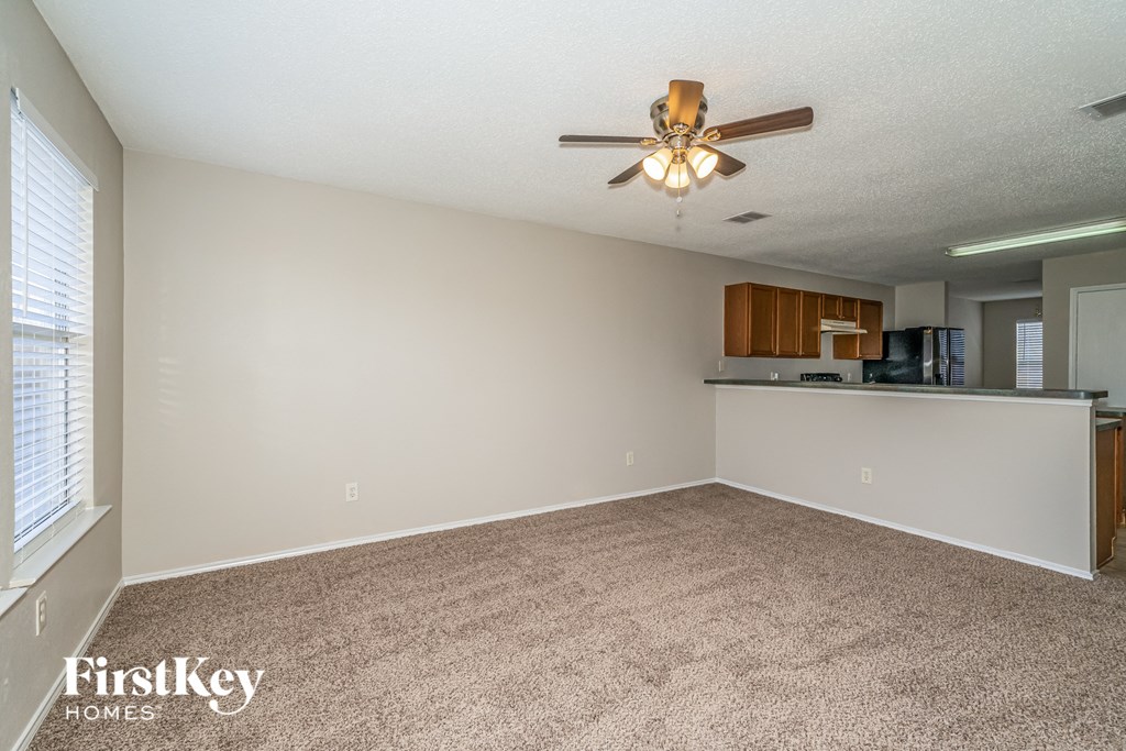 an empty living room with a ceiling fan and a kitchen