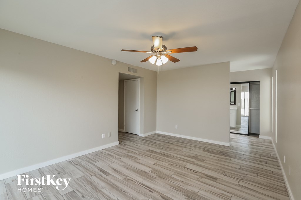 A spacious room with a ceiling fan and light fixture, and a wooden floor.