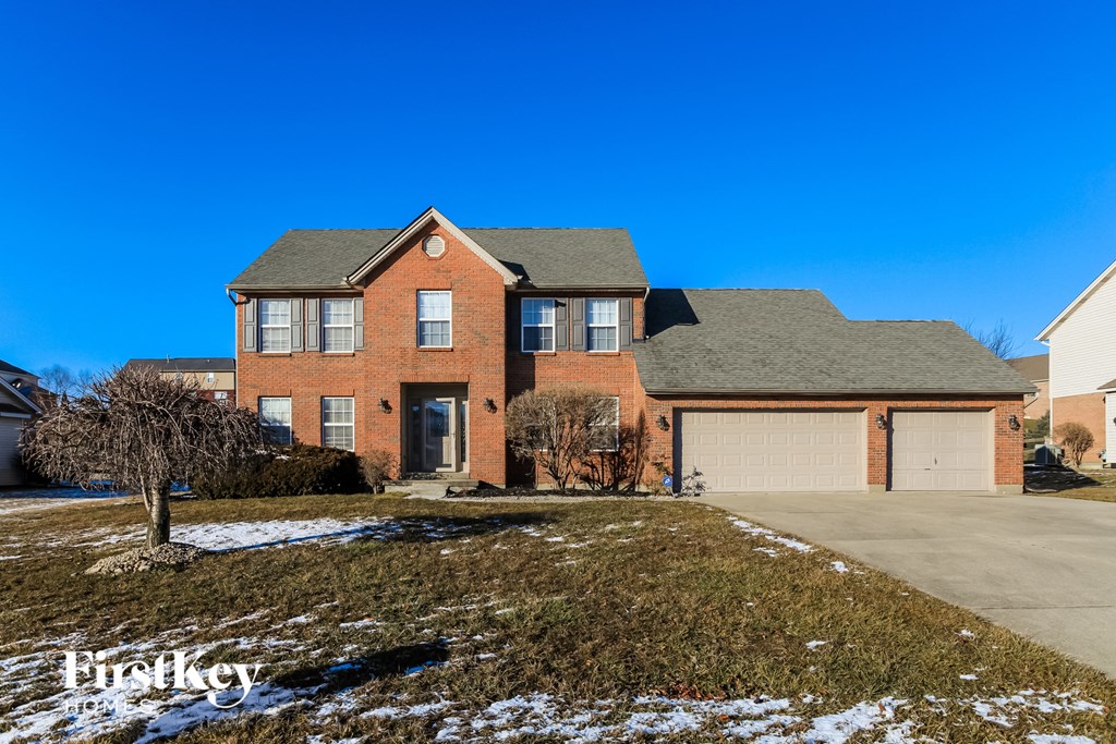 A large brick house with a garage and a tree in front.