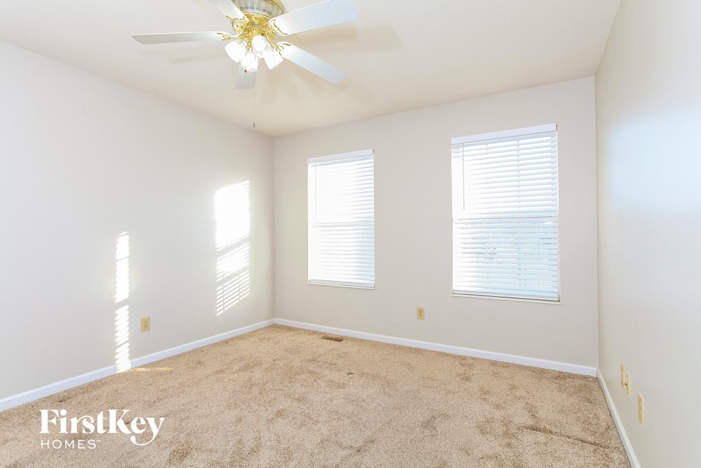 A room with a carpet floor, a ceiling fan, and two windows with blinds.