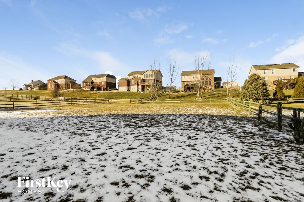 A snowy landscape with a wooden fence in the foreground and a row of houses in the background.
